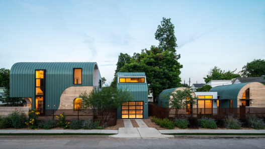 Modern architect-designed home with green curved metal roofs and warm interior lighting for the AIA Austin Homes Tour.